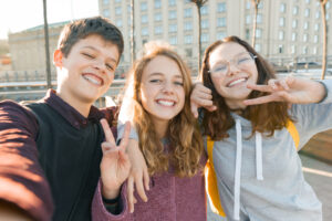 Tre glade ungdommer smiler til kameraet og viser vinnertegn.