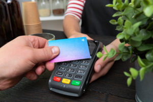 Hånd som holder betalingskortet oppå en betalingsterminal.