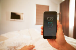 Hånd holder en klokkeapp på mobilteleson på et soverom.