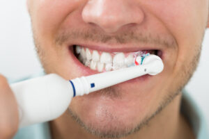 Mann børster tennene med elektrisk tannbørste.