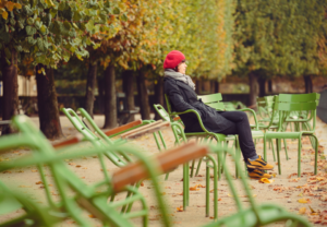 Kvinne som sitter i en park alene. Det er høst. Mange tomme stoler står rundt henne.