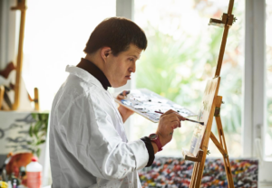 Ung mann maler bilde på lerret som er festet i staffeli.