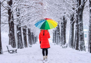  Jente spaserer i en vinterlig park med regnbueparaply.