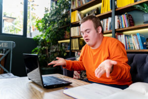 Un mann gestikulerer med hendene forran en PC. Han ser litt oppgitt ut.